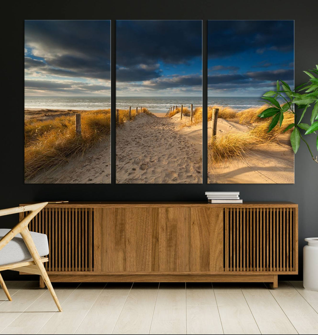 The Ocean Beach Dark Clouds Wall Art Canvas Print is a breathtaking triptych depicting a sandy beach path with tall grasses under an intense cloudy sky. It is crafted on museum-quality canvas with UV protection.