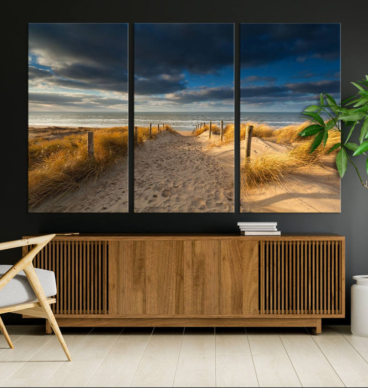 The Ocean Beach Dark Clouds Wall Art Canvas Print is a breathtaking triptych depicting a sandy beach path with tall grasses under an intense cloudy sky. It is crafted on museum-quality canvas with UV protection.