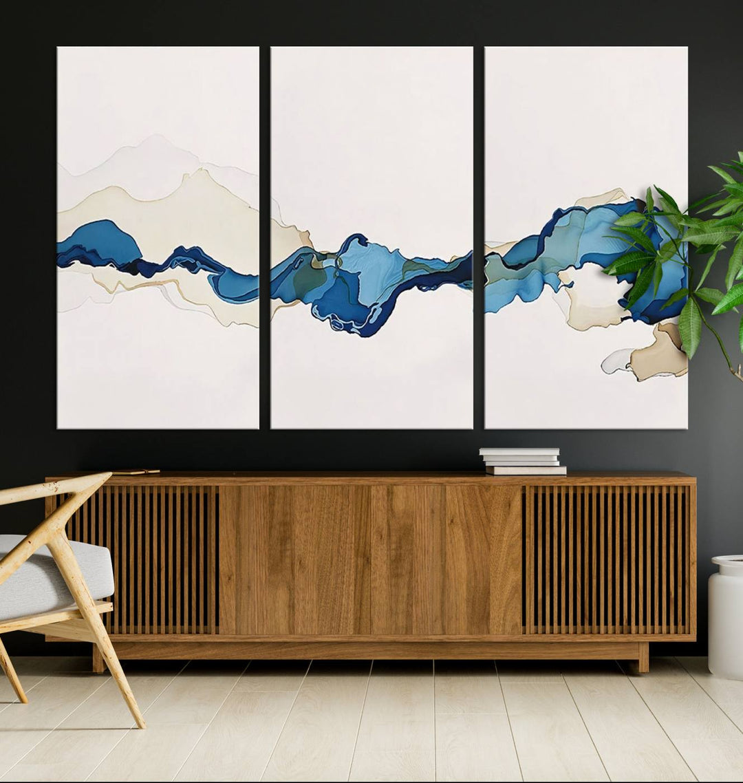 The modern living room showcases a set of three canvas prints with abstract blue art on museum-quality materials.