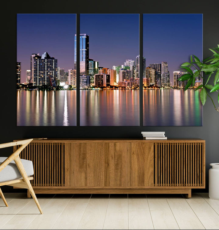 The Miami Skyline Canvas Wall Art Print showcases a vibrant night cityscape and beautifully captures the dazzling colorful lights reflecting on the water. This ready-to-hang triptych adorns the wall, creating a stunning visual centerpiece.