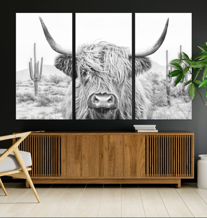 The "Rustic Charm | Cow Longhorn Black White Bighorn Wall Art Canvas Print" is a stunning triptych that showcases a highland cow with long horns set against a desert landscape with cacti in the background. This farmhouse wall art elevates any room into a rustic haven with its gallery-quality canvas.