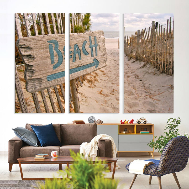 The Beach Is Calling You Wall Art Canvas Print features a sandy beach path with a wooden beach sign and arrow pointing to the ocean, beautifully displayed on museum-quality canvases.