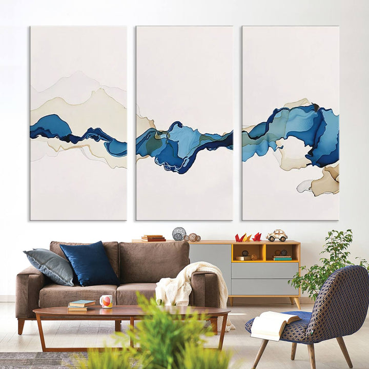 The modern living room showcases a set of three canvas prints with abstract blue art on museum-quality materials.