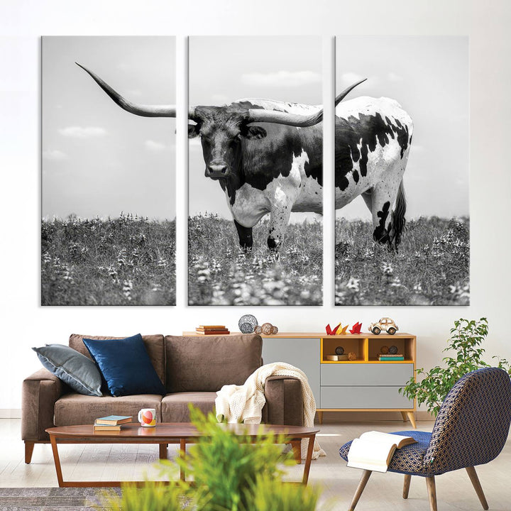 The Texas Black White Highland Longhorn Cow Wall Art Canvas Print, a gallery-quality triptych, elegantly adorns the wall, showcasing a striking black-and-white depiction of a longhorn cow in a field.