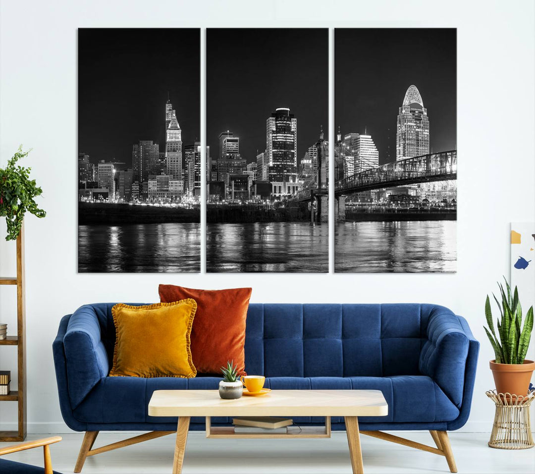 The Cincinnati City Lights Skyline Black and White Wall Art Cityscape Canvas Print elegantly adorns a modern living room. This museum-quality canvas triptych of a city skyline is enhanced by hand-assembled frames for added finesse, and you can enjoy free shipping on this stunning home addition.