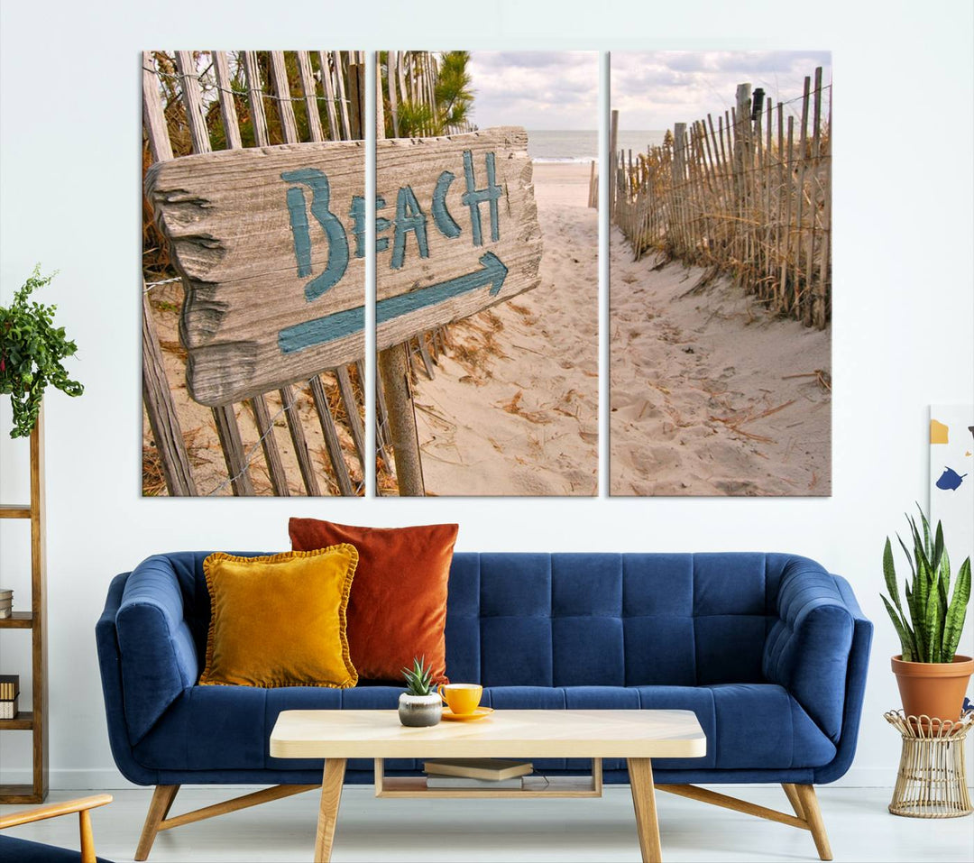 The Beach Is Calling You Wall Art Canvas Print features a sandy beach path with a wooden beach sign and arrow pointing to the ocean, beautifully displayed on museum-quality canvases.