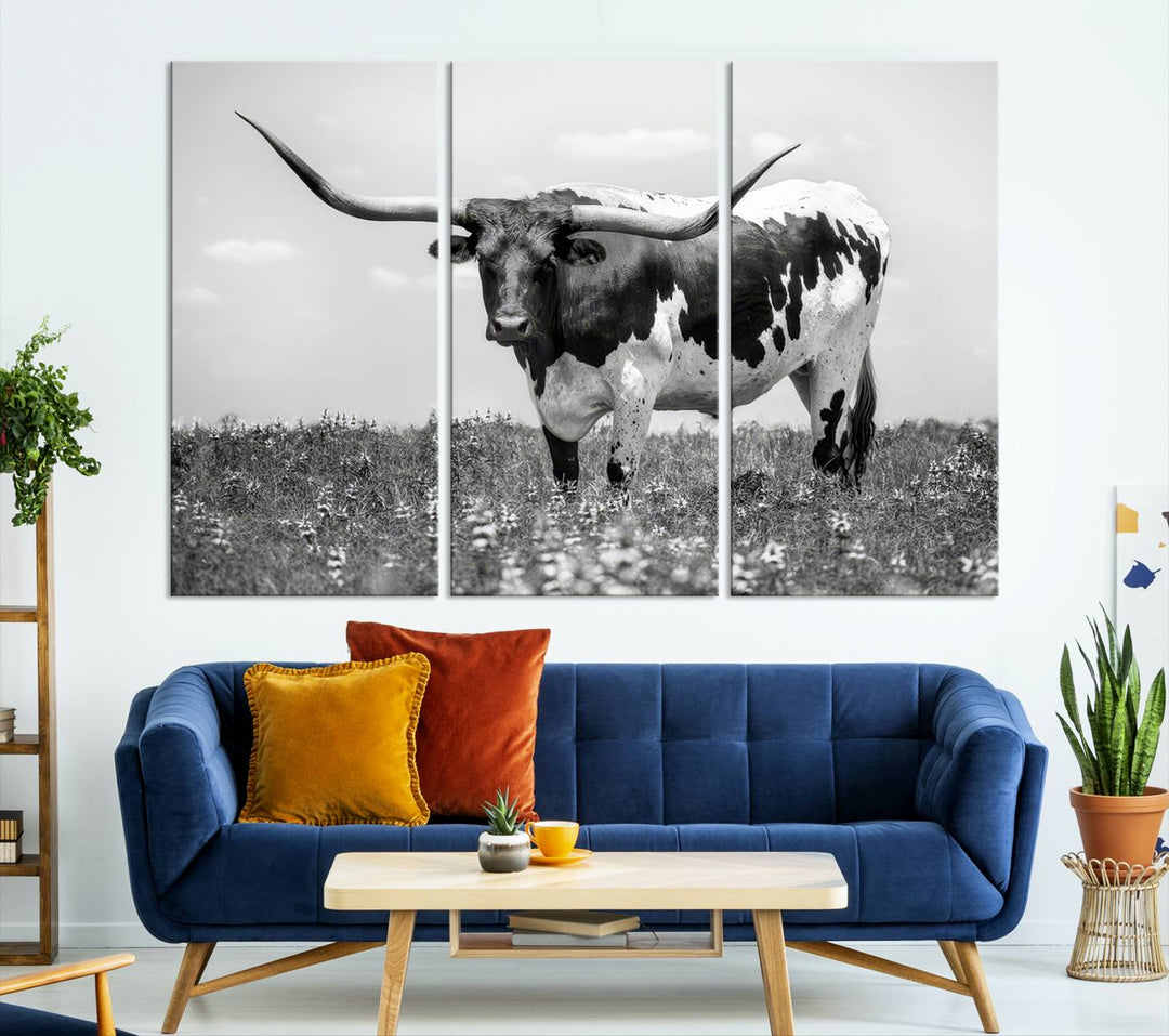 The Texas Black White Highland Longhorn Cow Wall Art Canvas Print, a gallery-quality triptych, elegantly adorns the wall, showcasing a striking black-and-white depiction of a longhorn cow in a field.