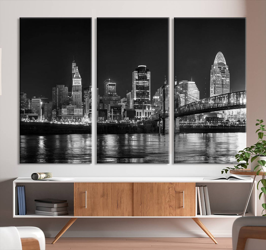 The Cincinnati City Lights Skyline Black and White Wall Art Cityscape Canvas Print elegantly adorns a modern living room. This museum-quality canvas triptych of a city skyline is enhanced by hand-assembled frames for added finesse, and you can enjoy free shipping on this stunning home addition.