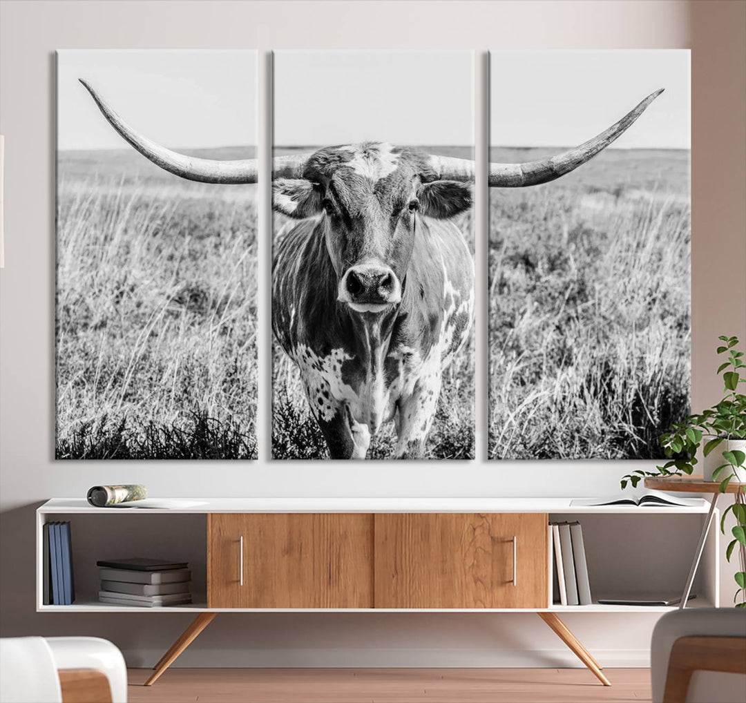 The Texas Cow Longhorn Wall Art Canvas Print is a black and white triptych depicting a cow in a field. It is crafted with museum-quality canvas and features a UV-protective coating.