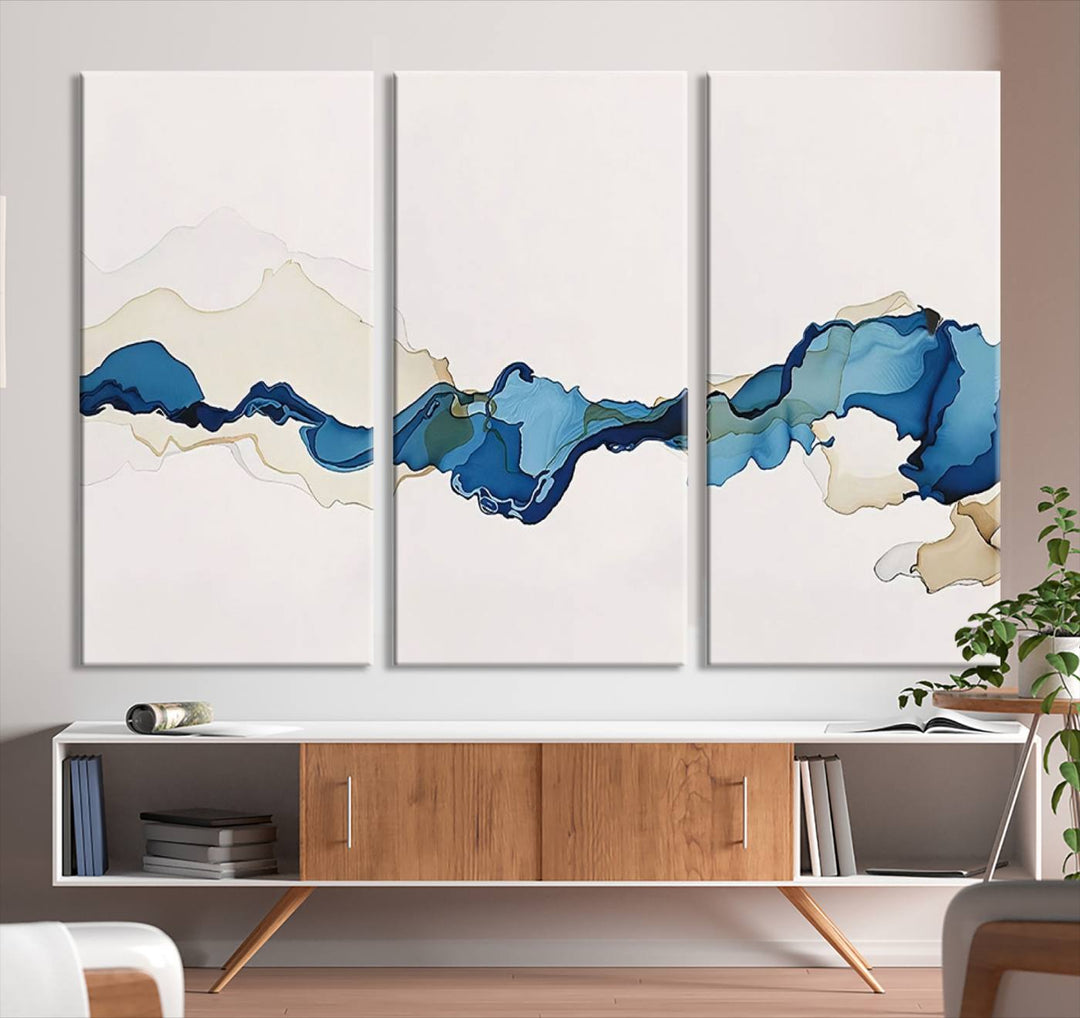 The modern living room showcases a set of three canvas prints with abstract blue art on museum-quality materials.