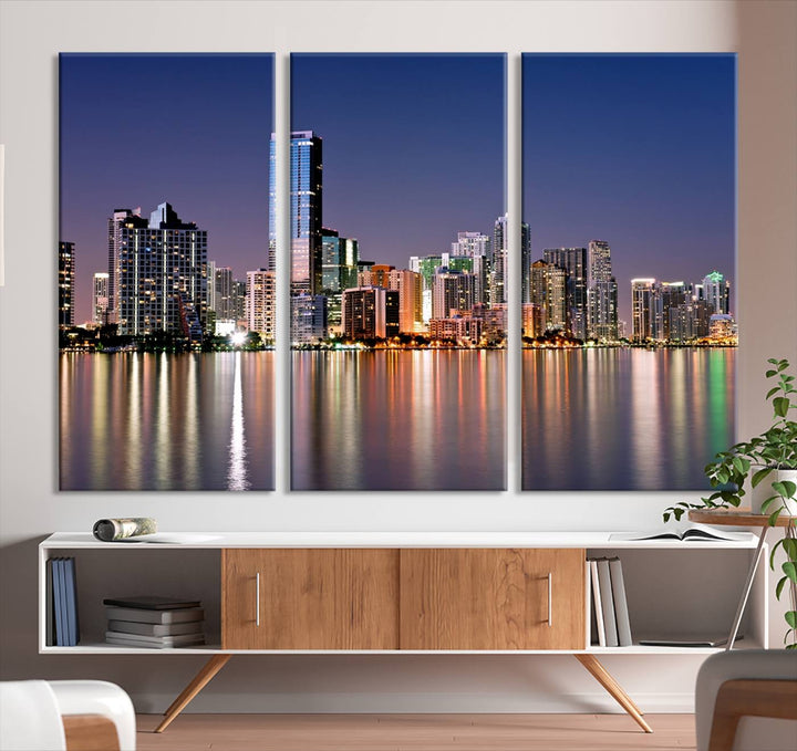 The Miami Skyline Canvas Wall Art Print showcases a vibrant night cityscape and beautifully captures the dazzling colorful lights reflecting on the water. This ready-to-hang triptych adorns the wall, creating a stunning visual centerpiece.