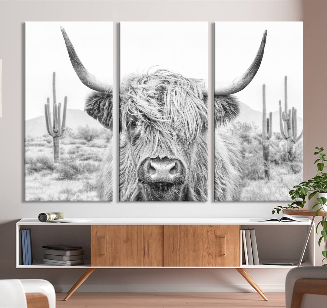 The "Rustic Charm | Cow Longhorn Black White Bighorn Wall Art Canvas Print" is a stunning triptych that showcases a highland cow with long horns set against a desert landscape with cacti in the background. This farmhouse wall art elevates any room into a rustic haven with its gallery-quality canvas.