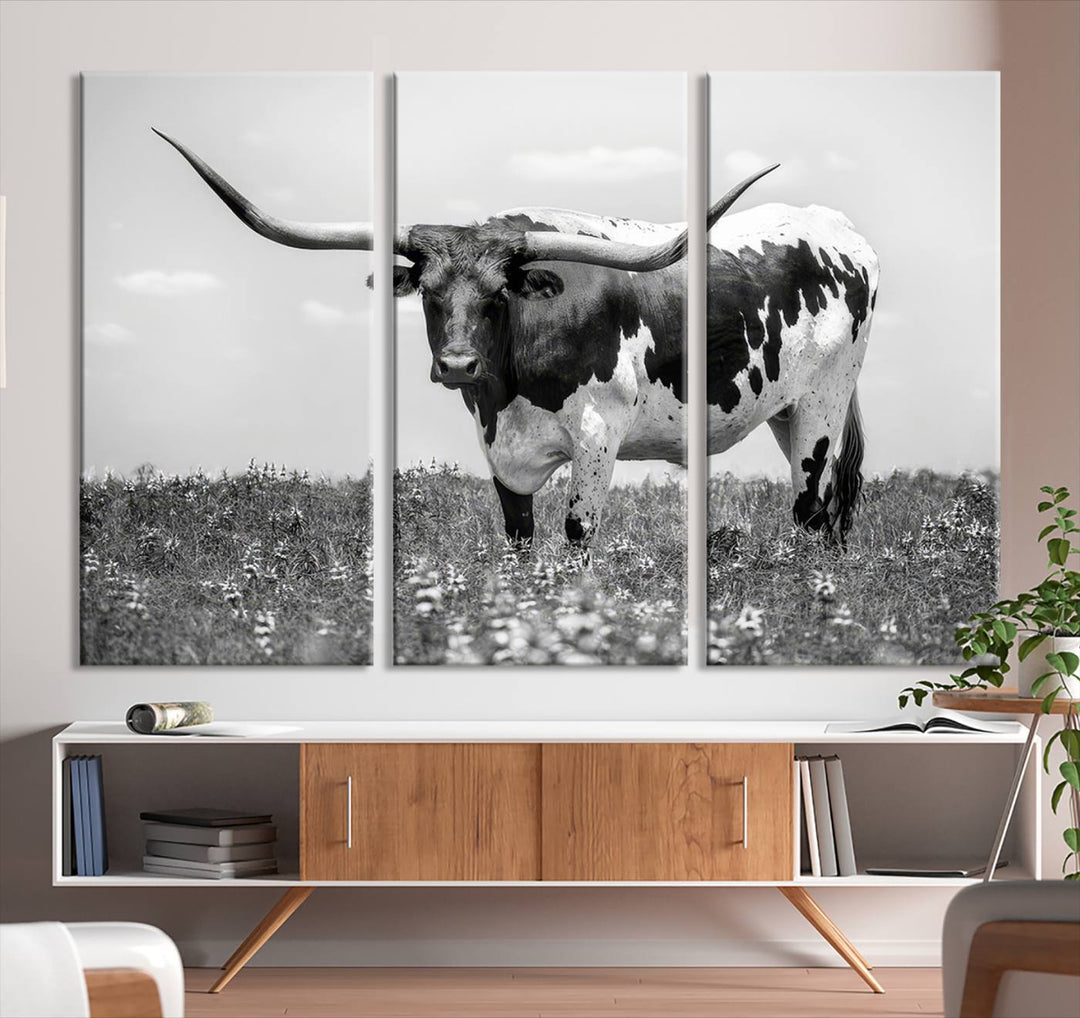 The Texas Black White Highland Longhorn Cow Wall Art Canvas Print, a gallery-quality triptych, elegantly adorns the wall, showcasing a striking black-and-white depiction of a longhorn cow in a field.