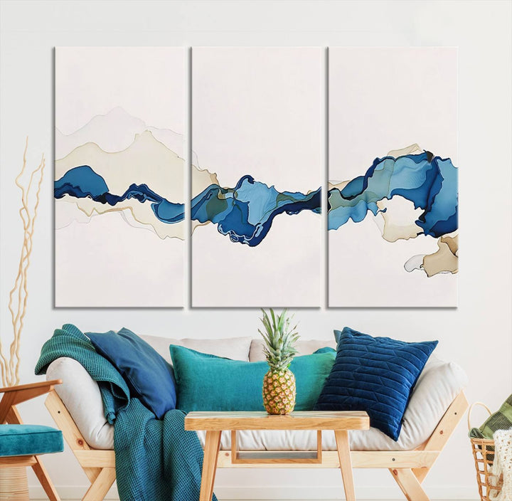 The modern living room showcases a set of three canvas prints with abstract blue art on museum-quality materials.