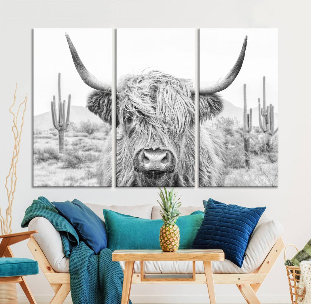 The "Rustic Charm | Cow Longhorn Black White Bighorn Wall Art Canvas Print" is a stunning triptych that showcases a highland cow with long horns set against a desert landscape with cacti in the background. This farmhouse wall art elevates any room into a rustic haven with its gallery-quality canvas.