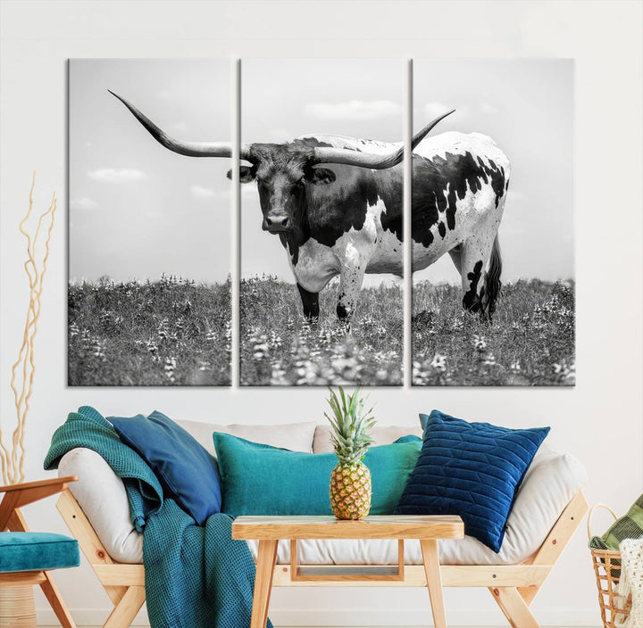 The Texas Black White Highland Longhorn Cow Wall Art Canvas Print, a gallery-quality triptych, elegantly adorns the wall, showcasing a striking black-and-white depiction of a longhorn cow in a field.