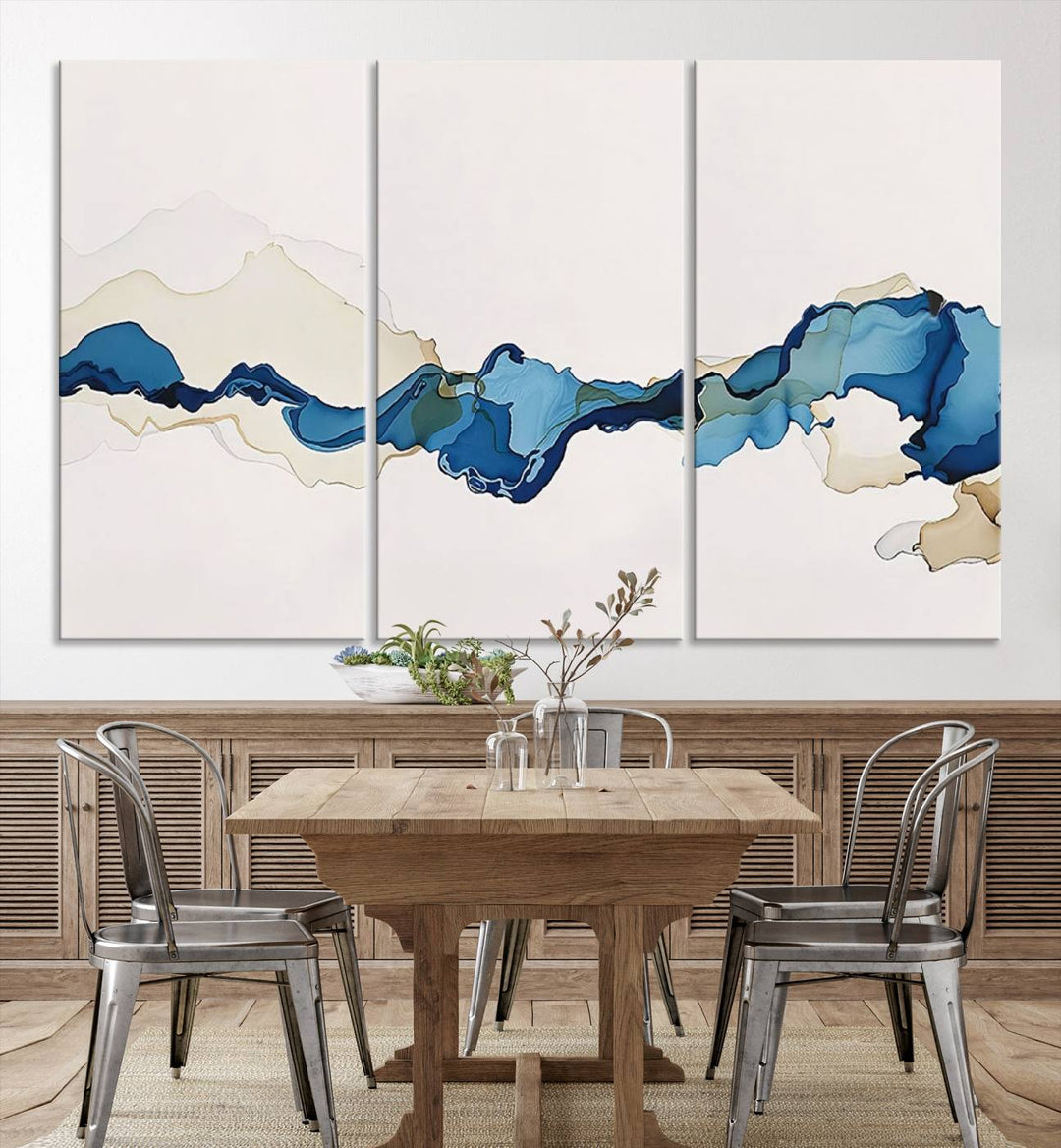 The modern living room showcases a set of three canvas prints with abstract blue art on museum-quality materials.