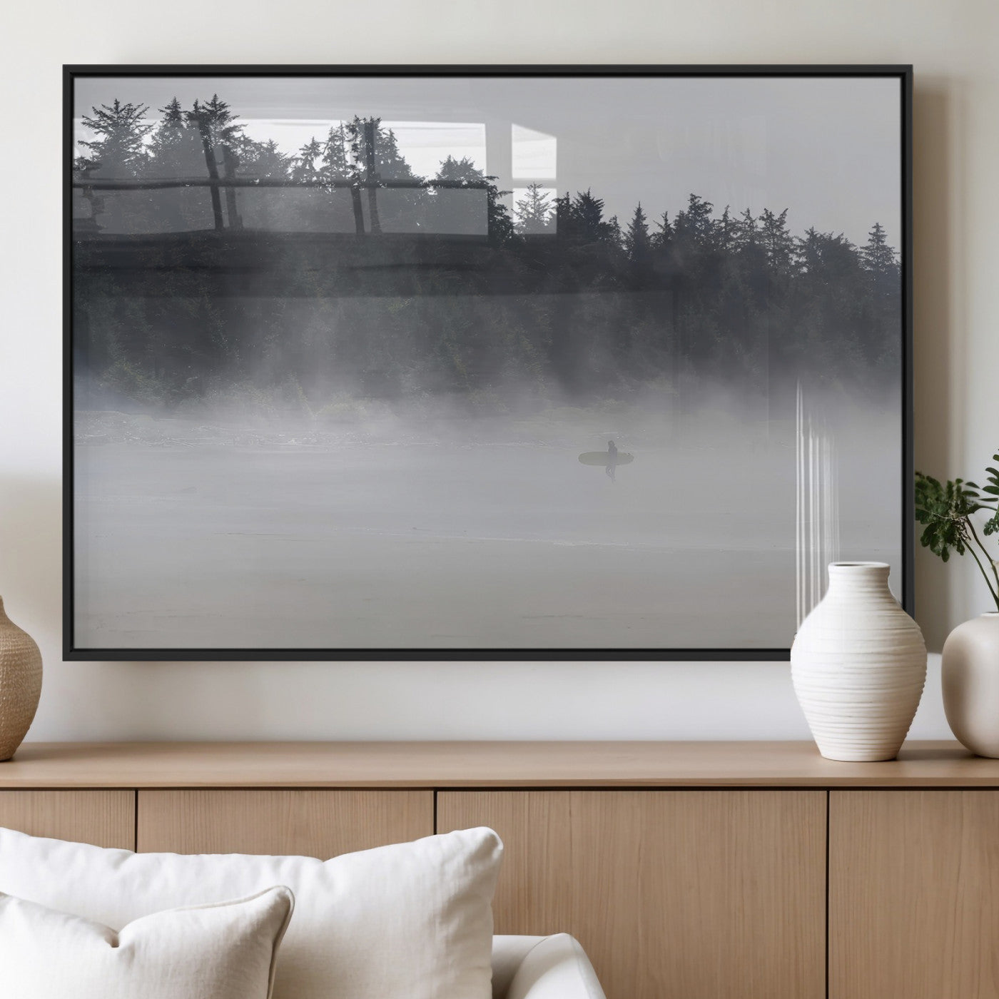 A lone surfer carrying a board through a misty shoreline, surrounded by dense trees and fog, creating a peaceful and mysterious coastal scene.