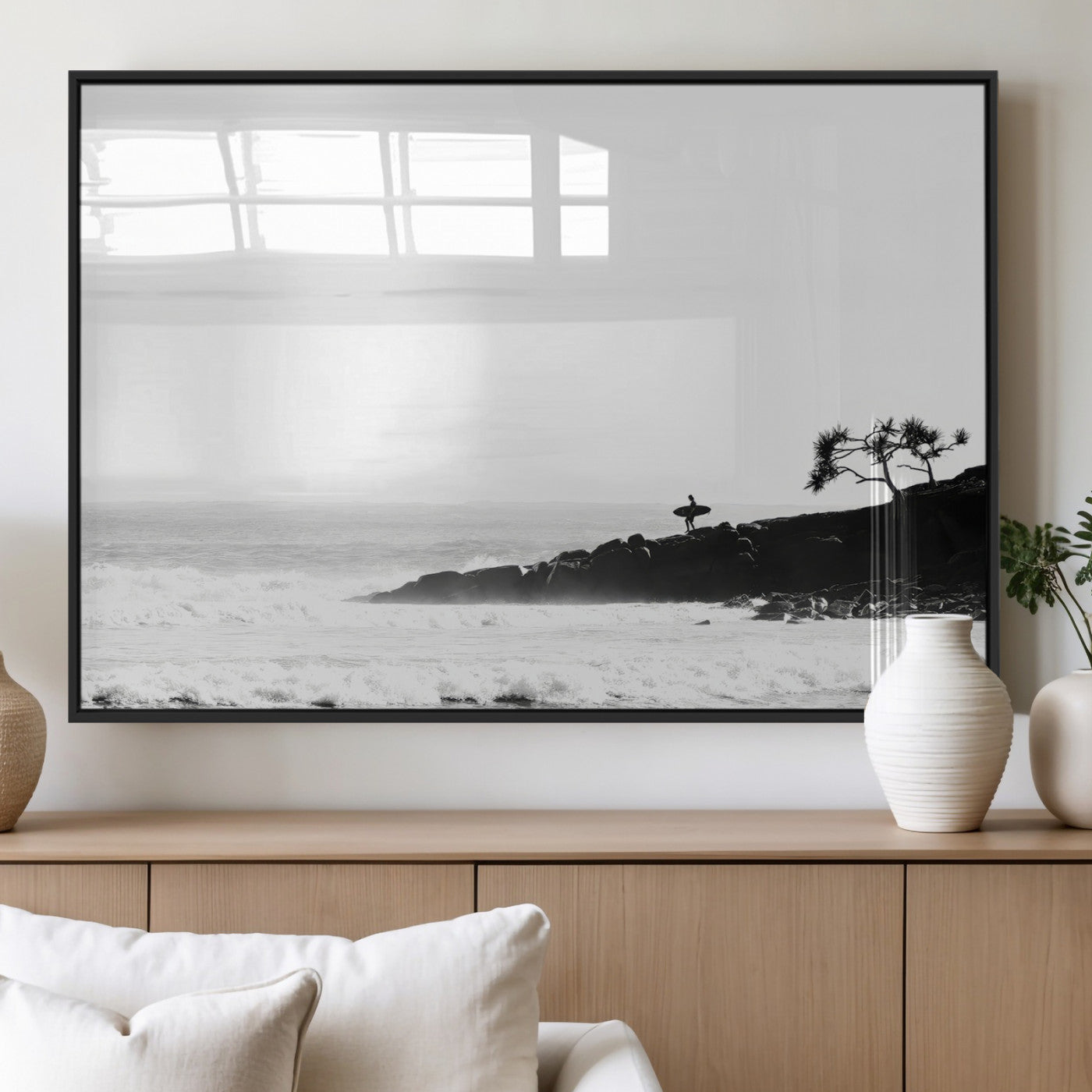 Black and white photo of a surfer standing on rocky cliffs, gazing at the waves, embodying the spirit of adventure and solitude.