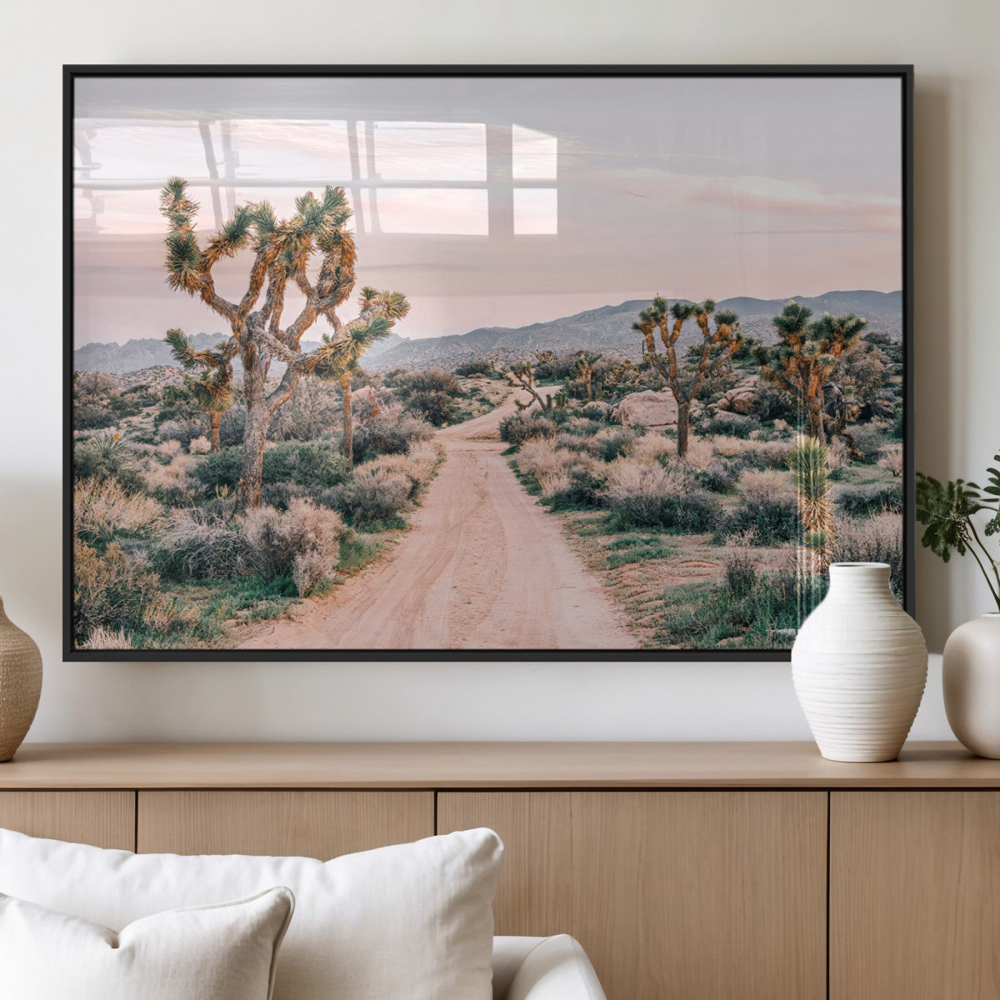 A dusty road winding through Joshua Tree National Park, framed by iconic twisted trees and warm desert tones under a soft pastel sky.