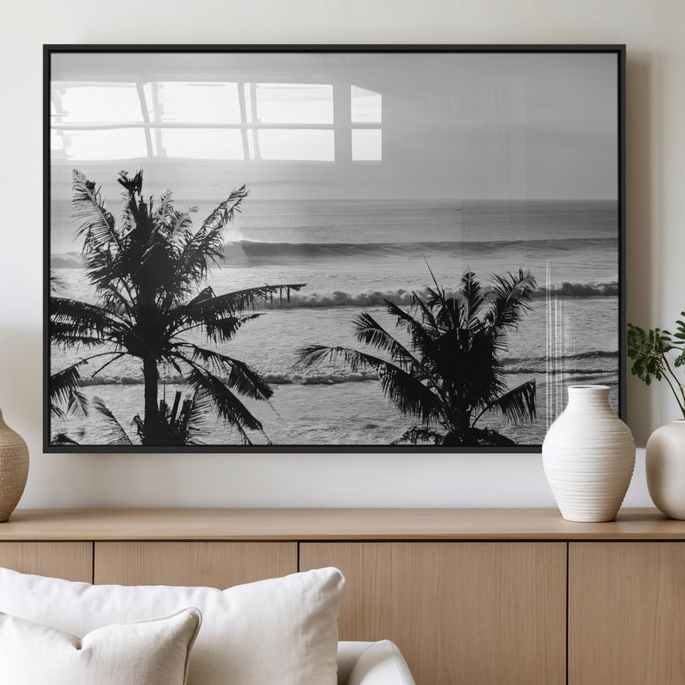 Black and white view of ocean waves crashing on a tropical coastline, framed by silhouetted palm trees under a vast, open sky.