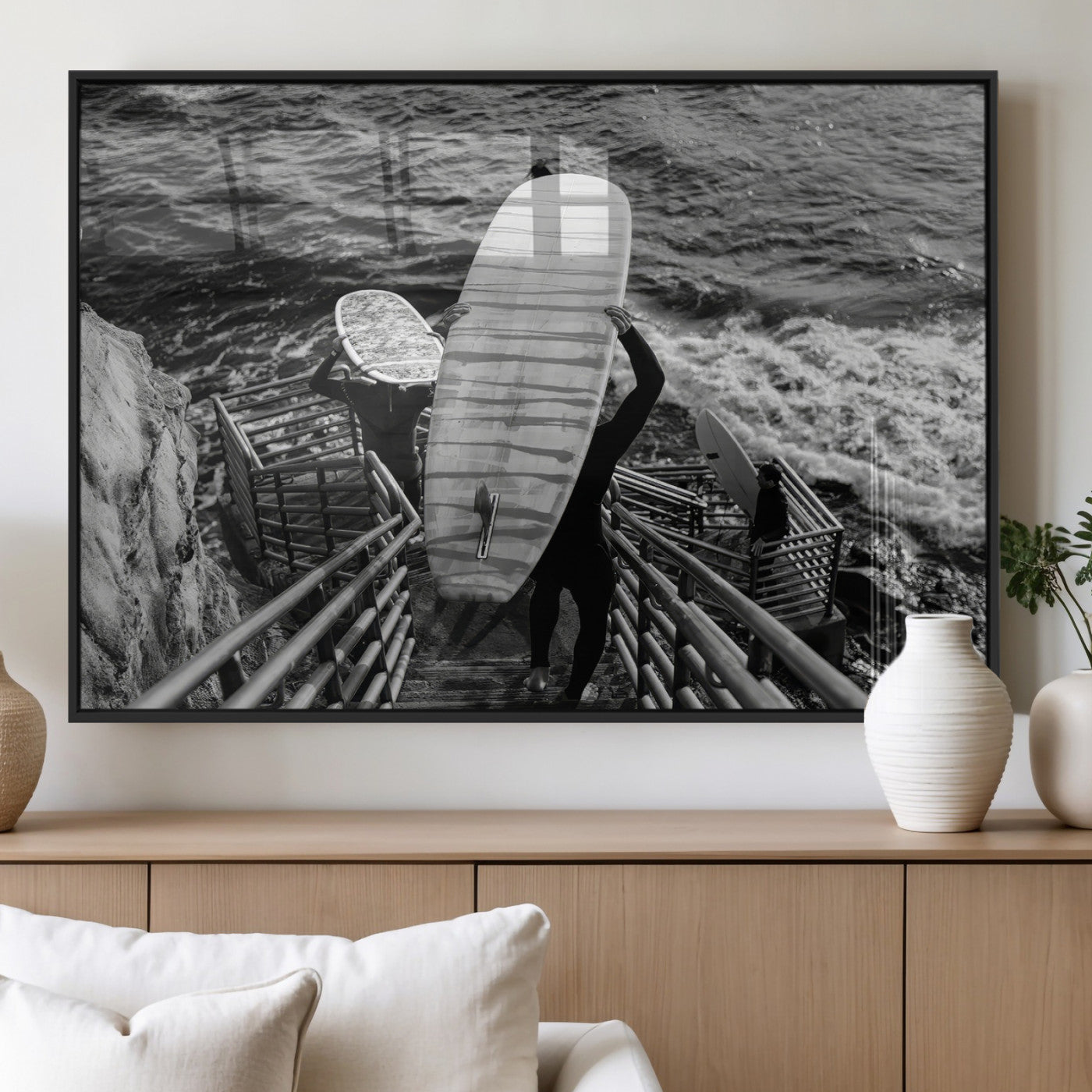 Black and white photo of surfers carrying boards down a rugged cliffside stairway, capturing a bold and adventurous coastal scene.