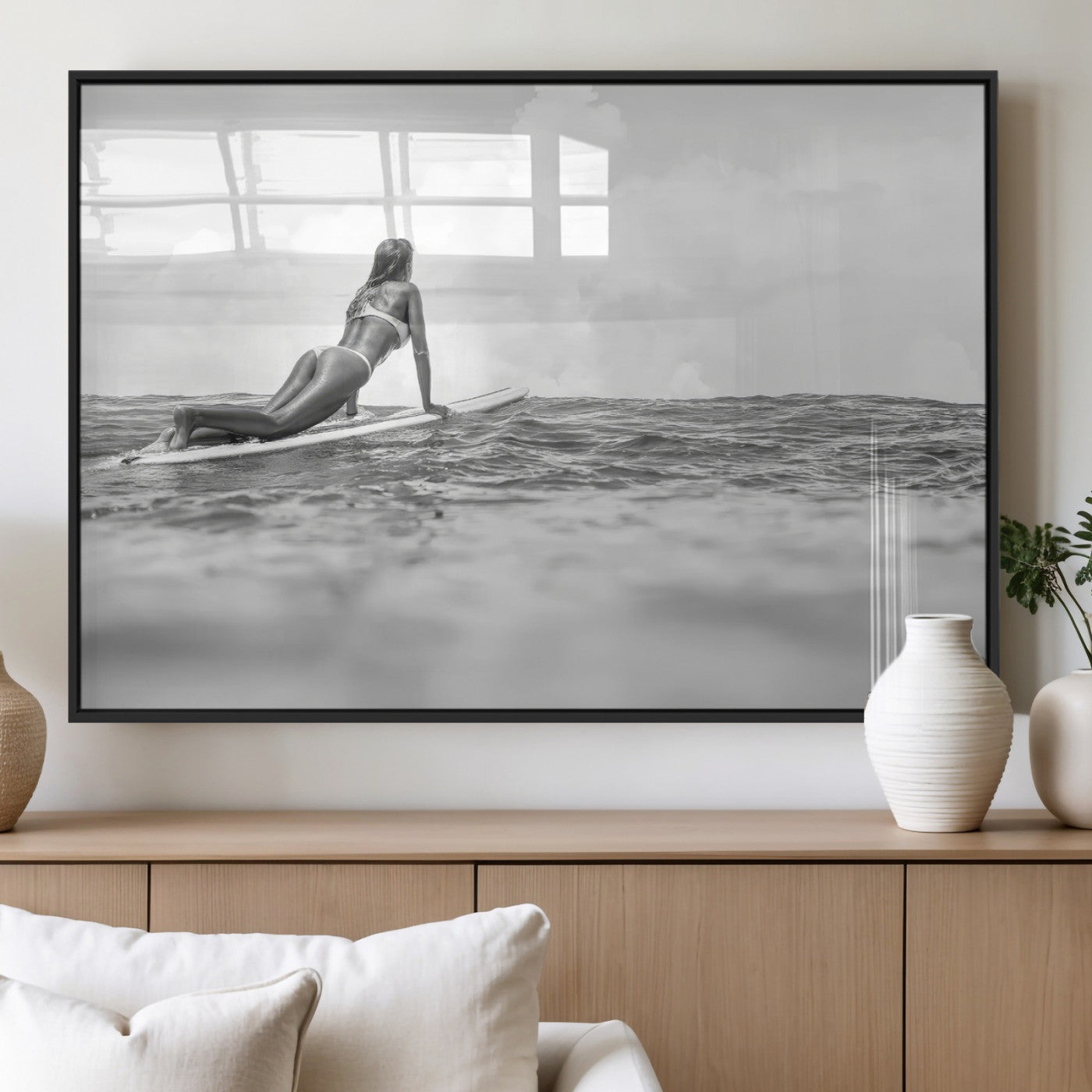 A black and white ocean scene featuring a surfer girl waiting on her board, gazing at the horizon, capturing a tranquil and adventurous coastal moment.