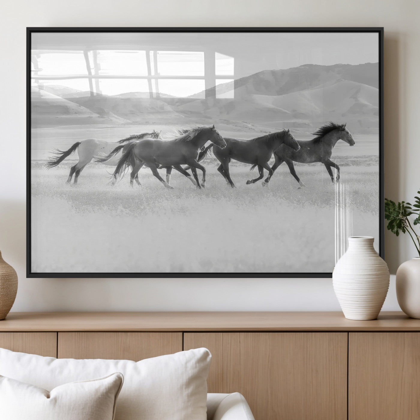 A black and white image of wild horses running freely across an open grassland, capturing the power and beauty of untamed nature in a rustic western setting.