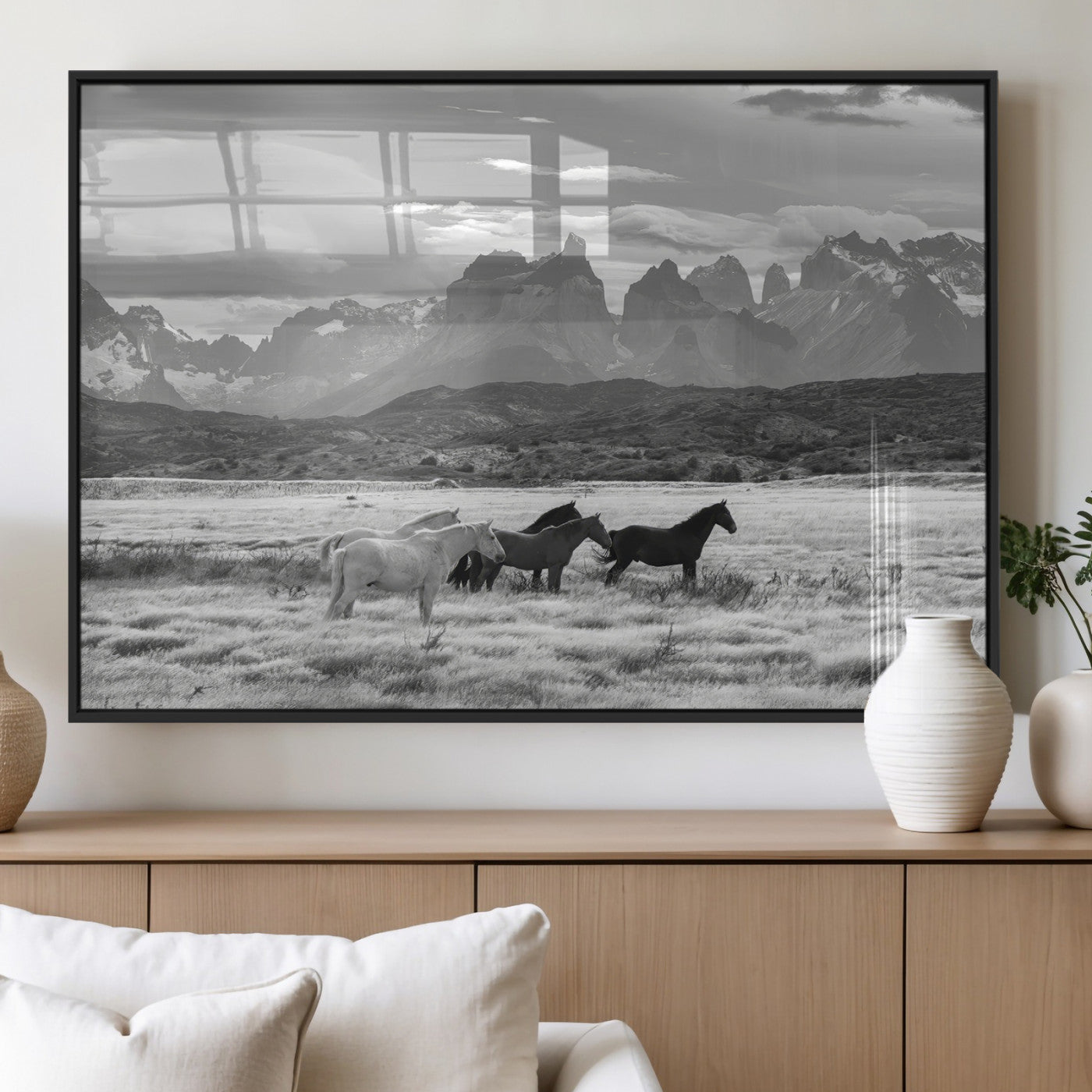 A black and white landscape of wild horses grazing in a vast grassland with towering mountains in the background, creating a moody and rustic western aesthetic.