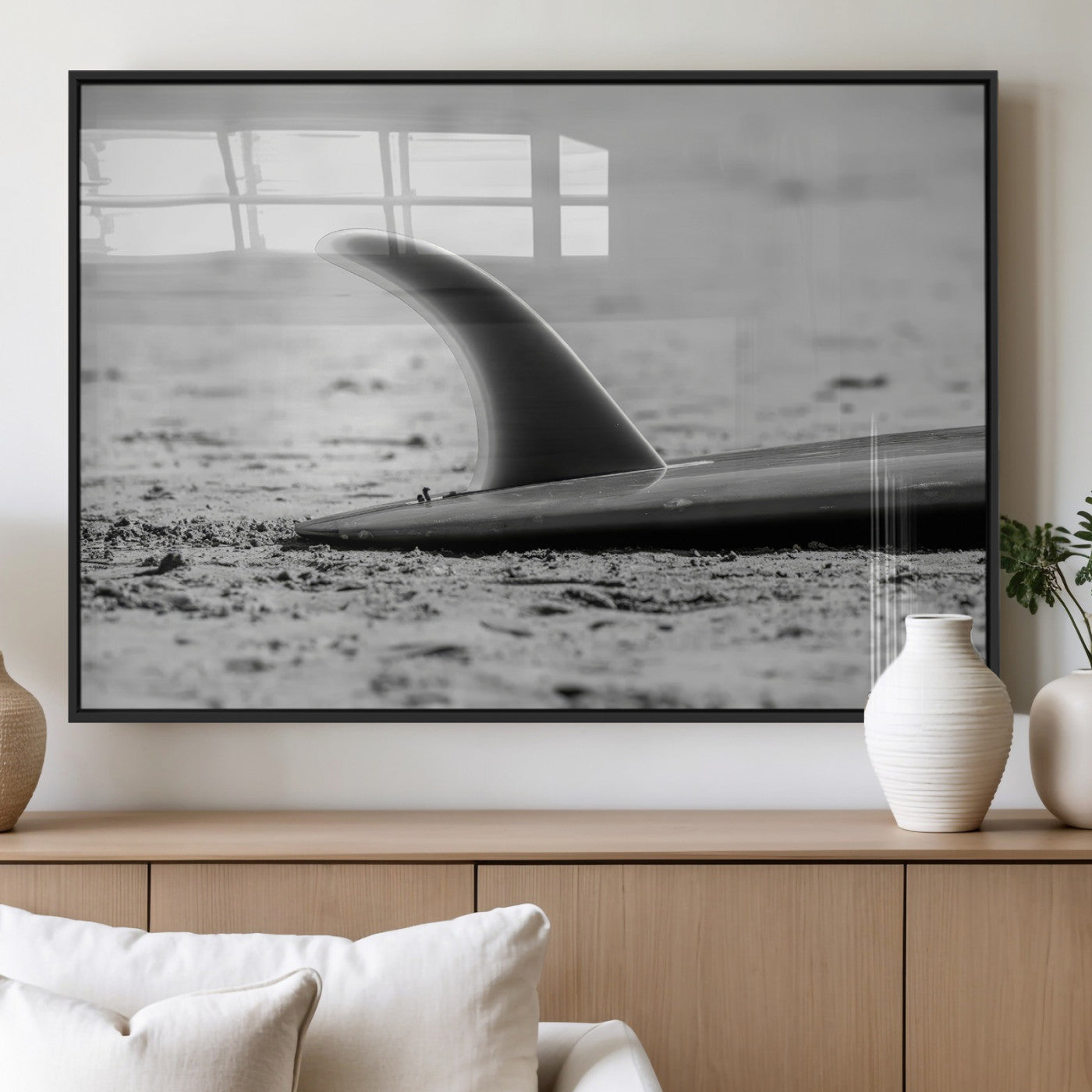 A black and white close-up of a surfboard fin resting on the sandy shore, highlighting minimalist beach aesthetics and classic surf culture.