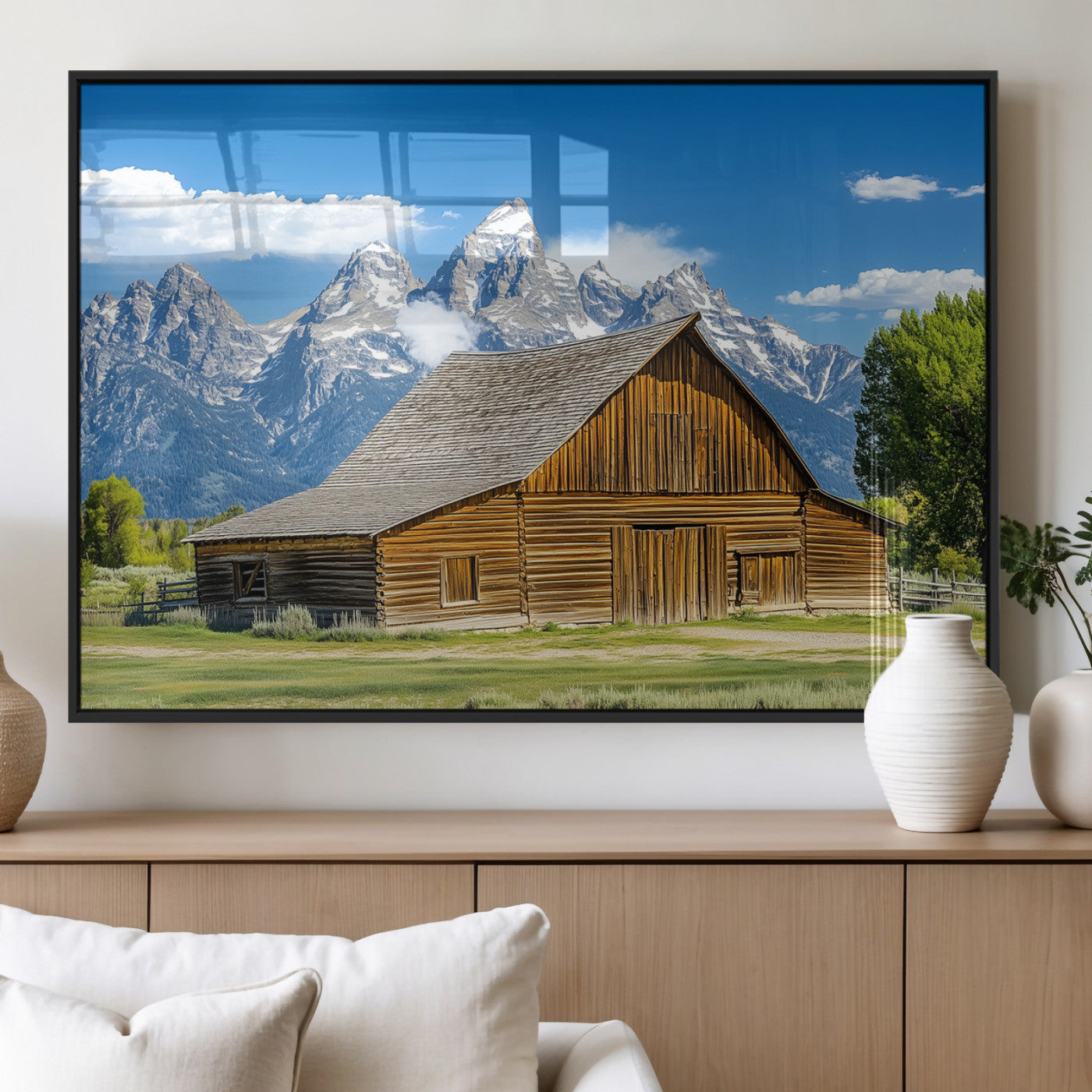 A rustic wooden barn sits in front of towering mountain peaks under a clear blue sky, perfect for farmhouse or cabin style interiors.