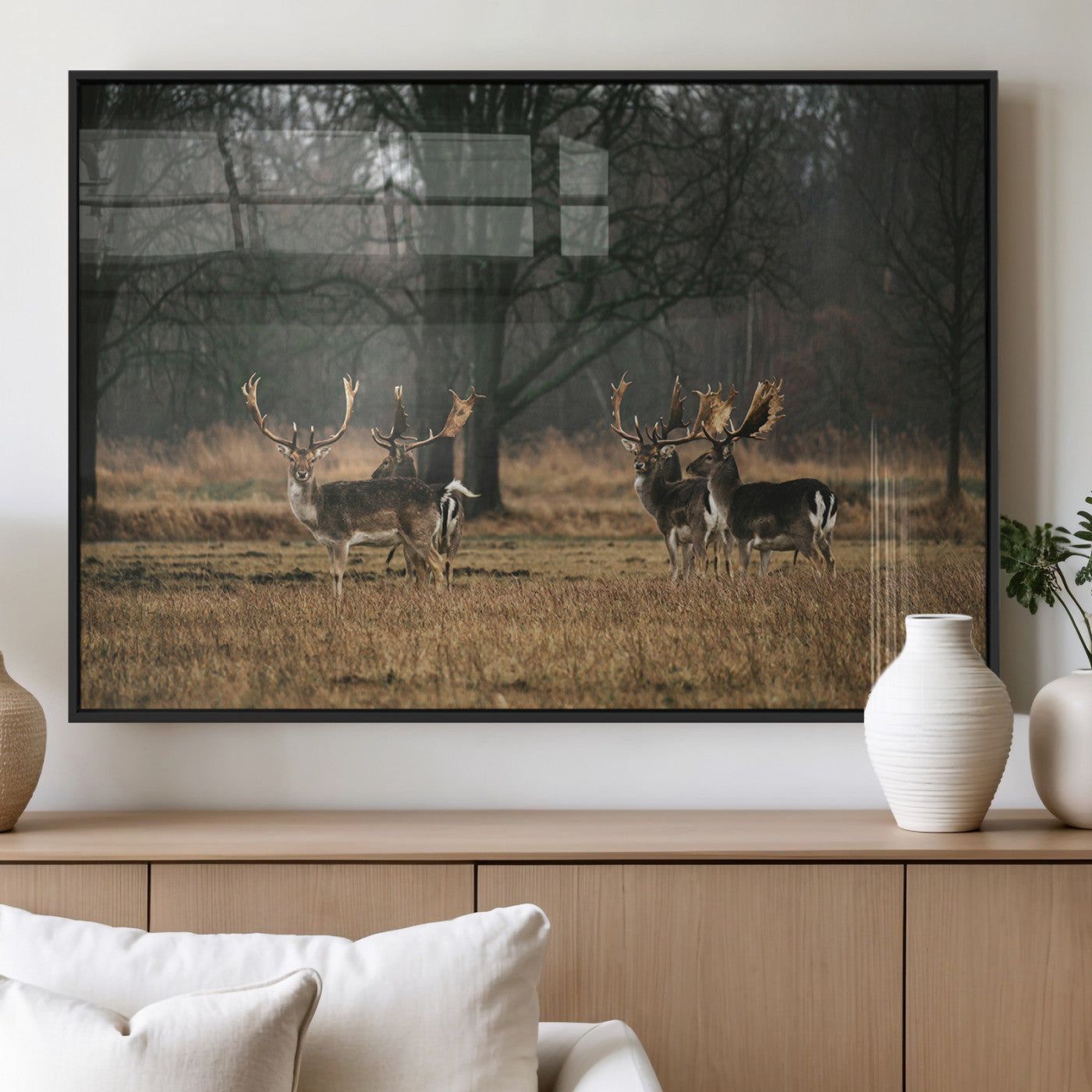 A group of majestic deer standing in a golden field with bare trees in the background, creating a peaceful woodland scene.