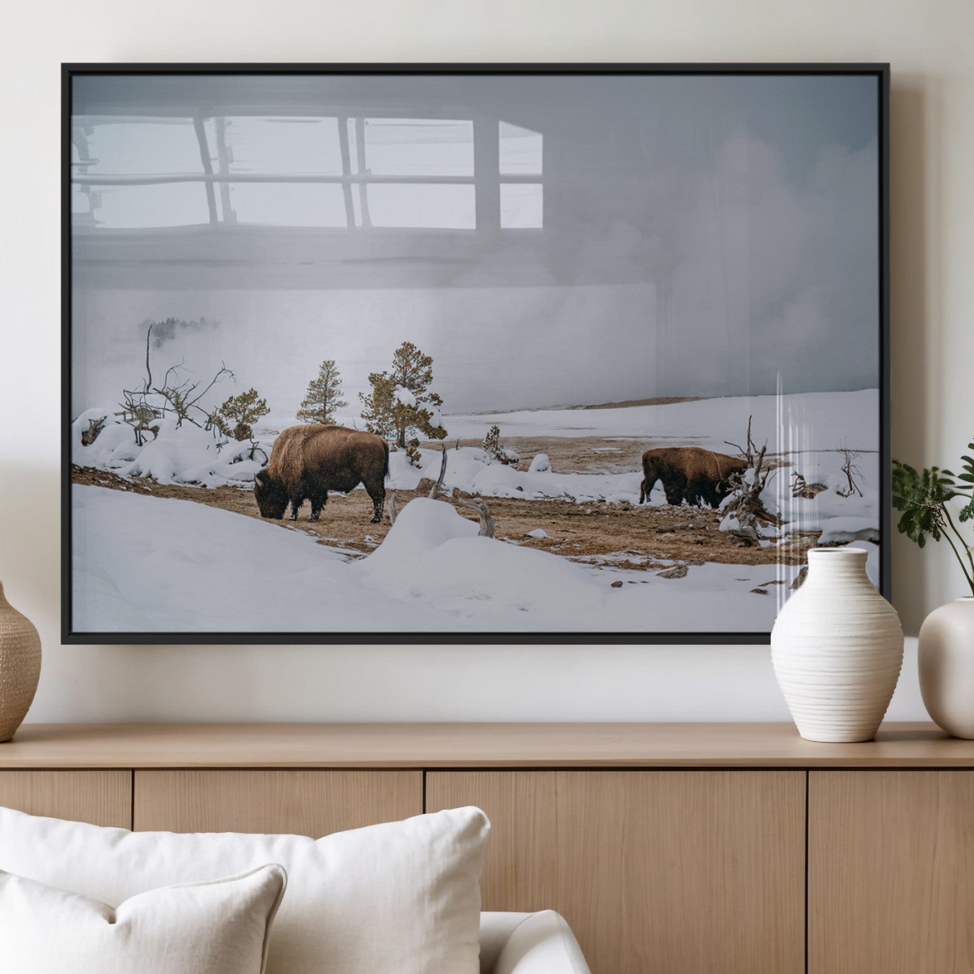 Two bison grazing in a snowy open landscape with misty hills in the background, creating a peaceful and rustic winter scene.