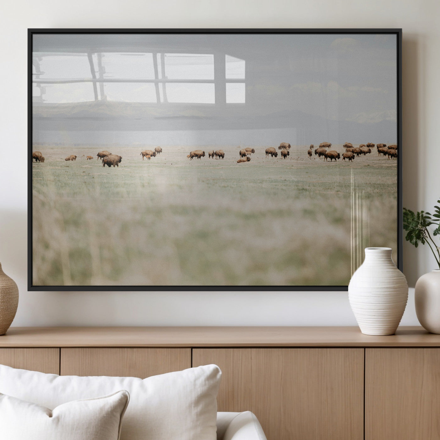 A herd of bison grazing in an open prairie with distant mountains under a soft sky, creating a serene and rustic Western landscape.