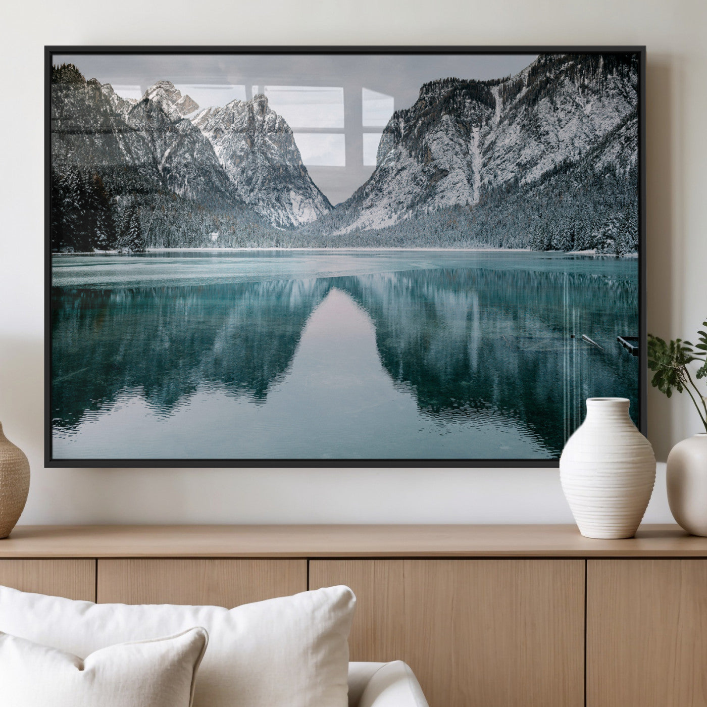 Crystal-clear alpine lake reflecting snow-covered mountains, surrounded by evergreen trees, creating a serene and tranquil winter landscape.