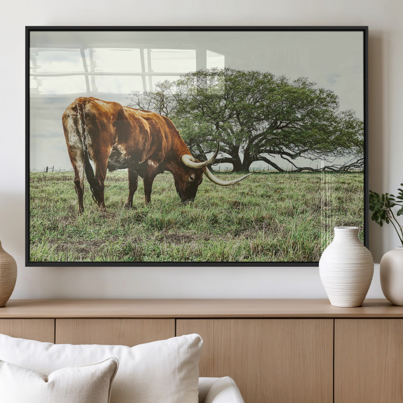 A Texas Longhorn grazing in a green pasture with a large tree in the background, evoking a rustic Western and farmhouse aesthetic.