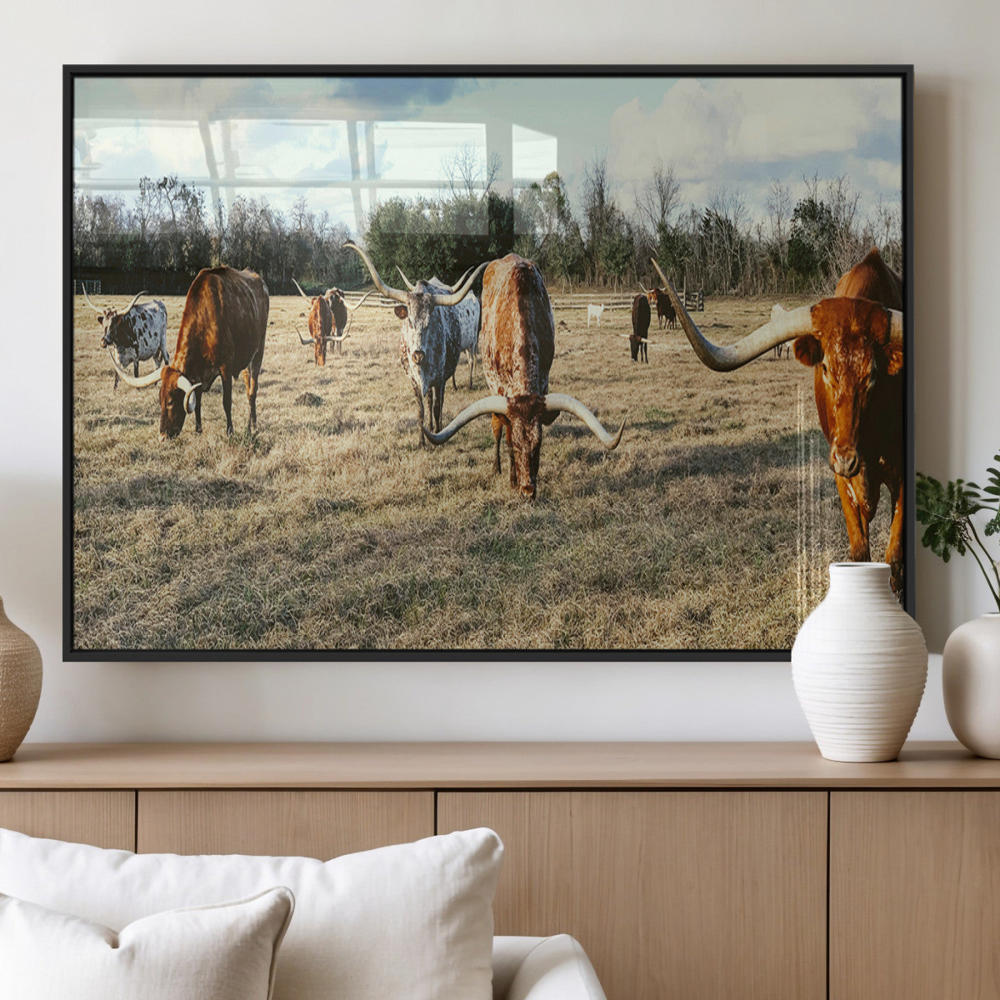 A herd of Texas Longhorn cattle grazing in an open field under a partly cloudy sky, capturing a rustic and Western ranch aesthetic.