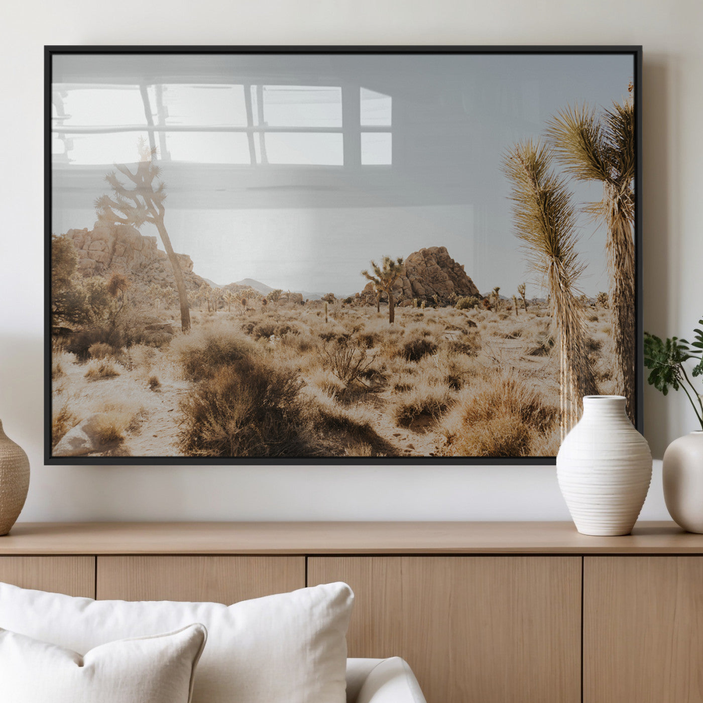 Sunlit desert landscape featuring Joshua trees, rocky formations, and dry bushes under a clear sky.