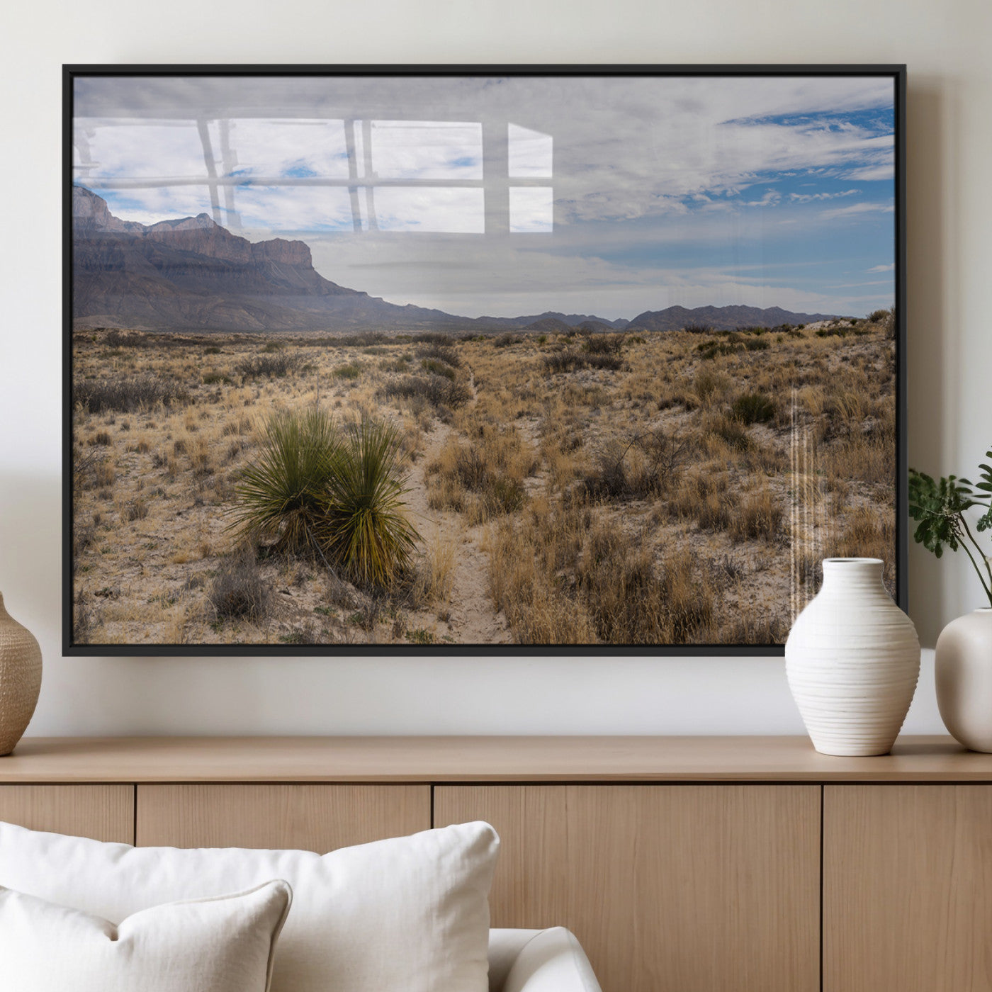 A scenic desert landscape with dry grasses, scattered shrubs, and a distant mountain range under a partly cloudy blue sky.