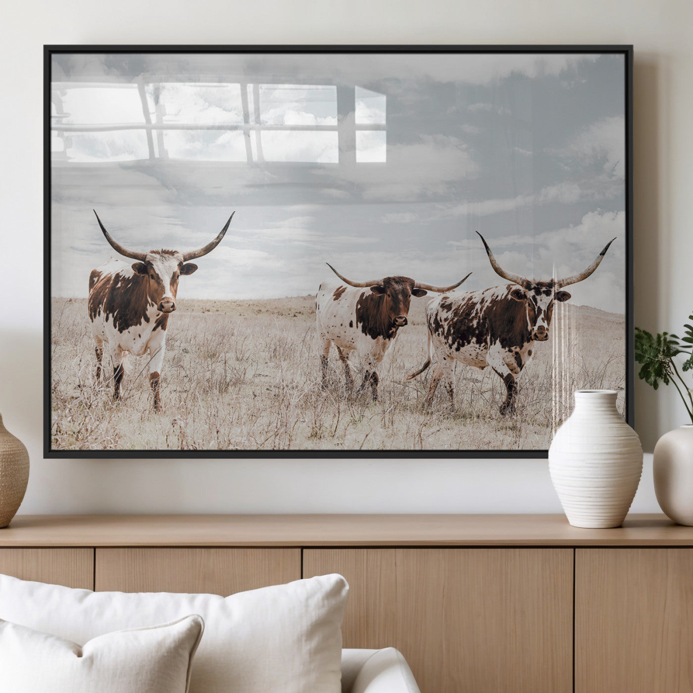 Three Texas Longhorn cattle walking through a dry grassy field under a partly cloudy sky.