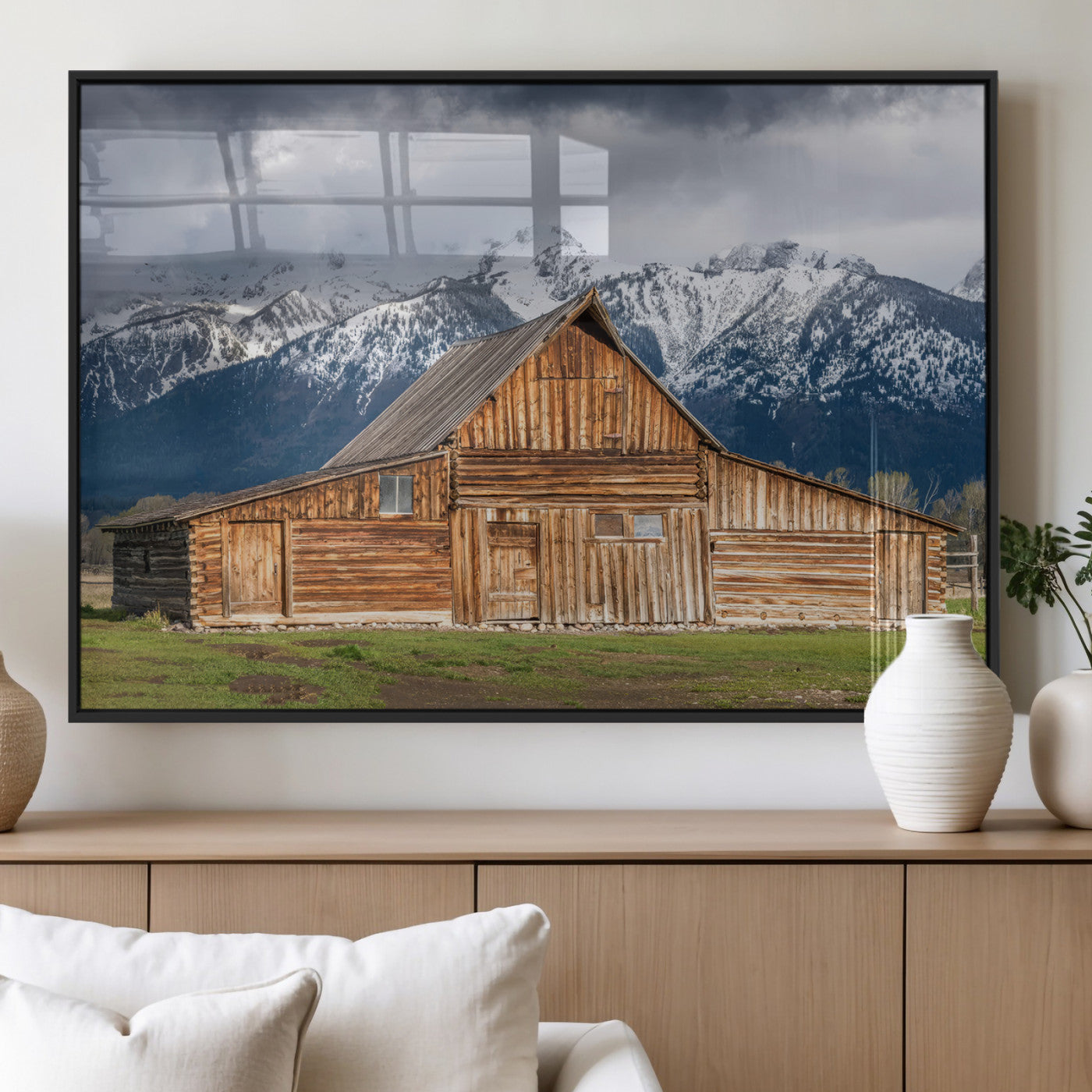A stunning wall art canvas print featuring a rustic wooden barn set against a backdrop of snow-capped mountains under a dramatic cloudy sky, perfect for adding a touch of rural charm to any space.