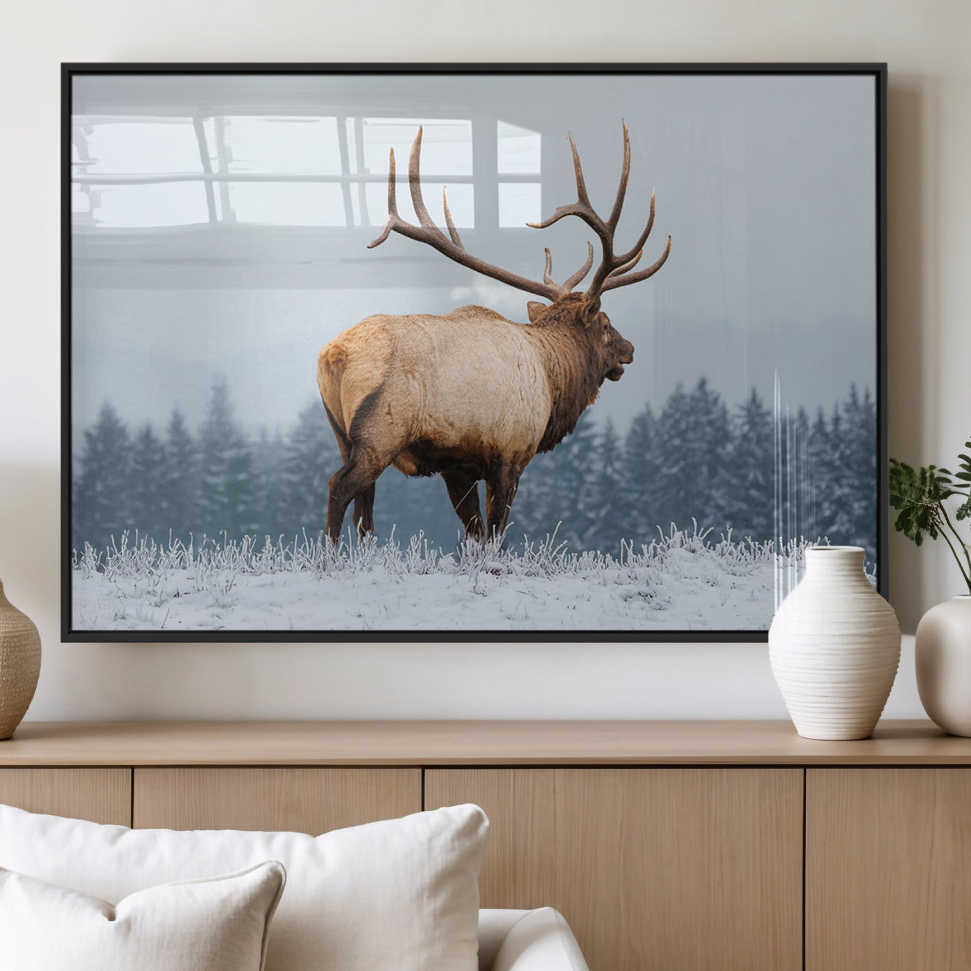 A majestic elk standing in a snowy landscape, with large antlers, set against a backdrop of evergreen trees and a soft winter sky.