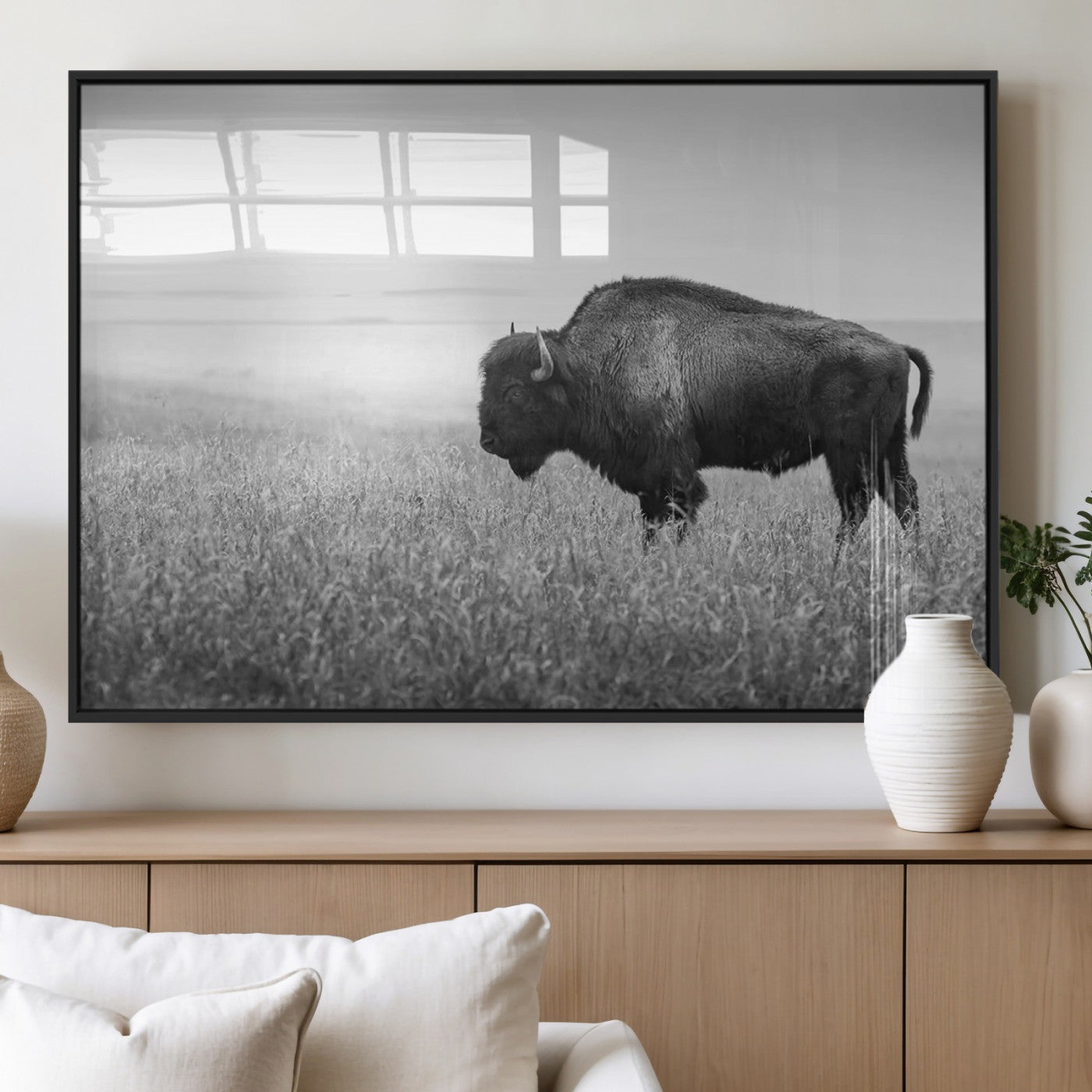 "Black and white image of a bison grazing in a vast field under an overcast sky."