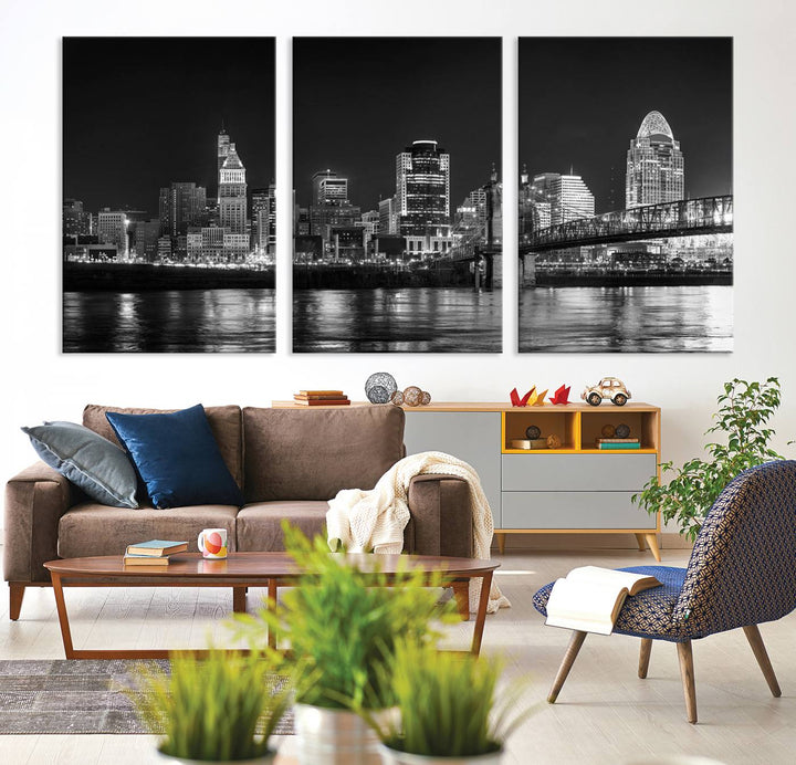 The Cincinnati City Lights Skyline Black and White Wall Art Cityscape Canvas Print elegantly adorns a modern living room. This museum-quality canvas triptych of a city skyline is enhanced by hand-assembled frames for added finesse, and you can enjoy free shipping on this stunning home addition.