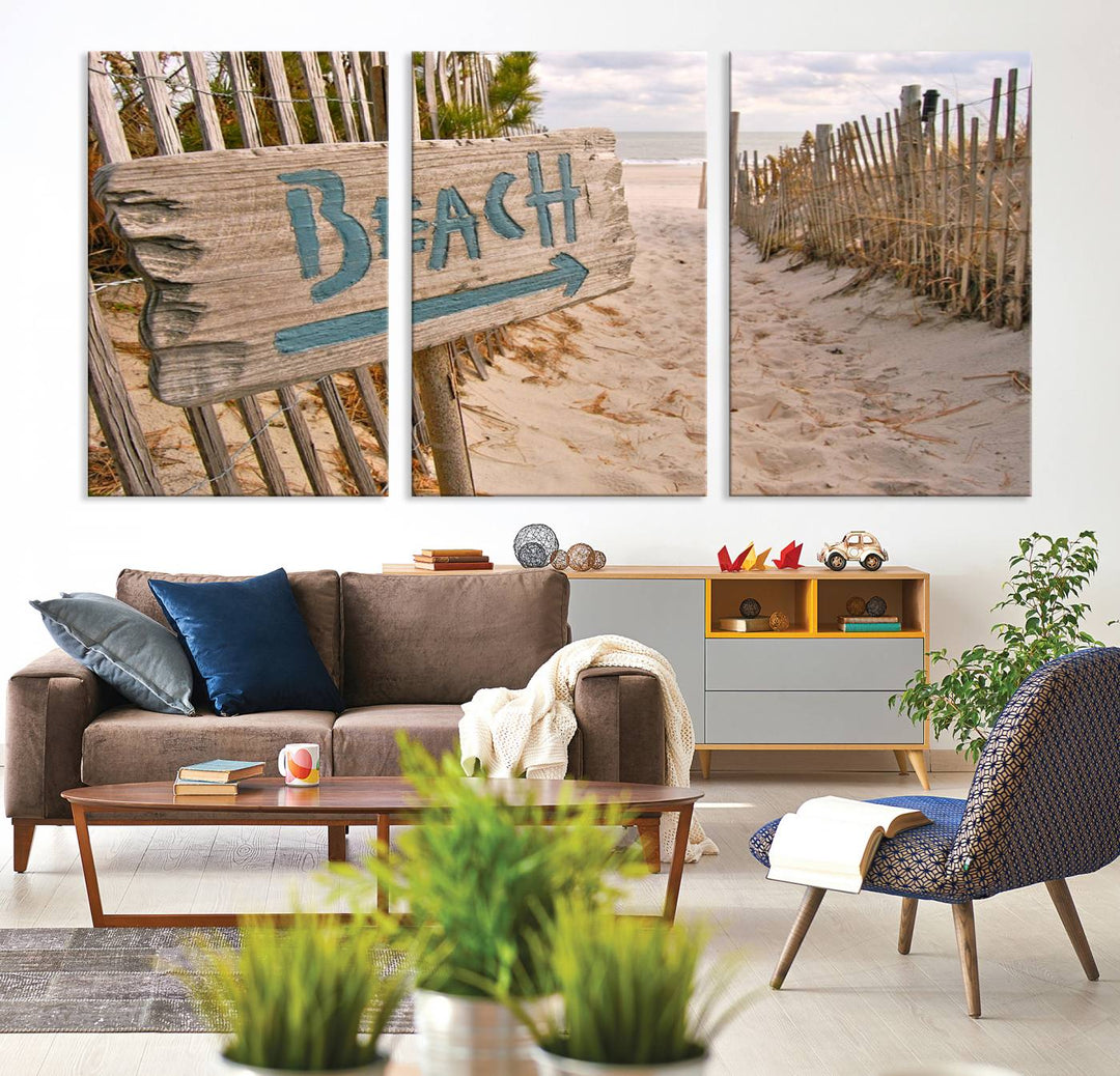 The Beach Is Calling You Wall Art Canvas Print features a sandy beach path with a wooden beach sign and arrow pointing to the ocean, beautifully displayed on museum-quality canvases.