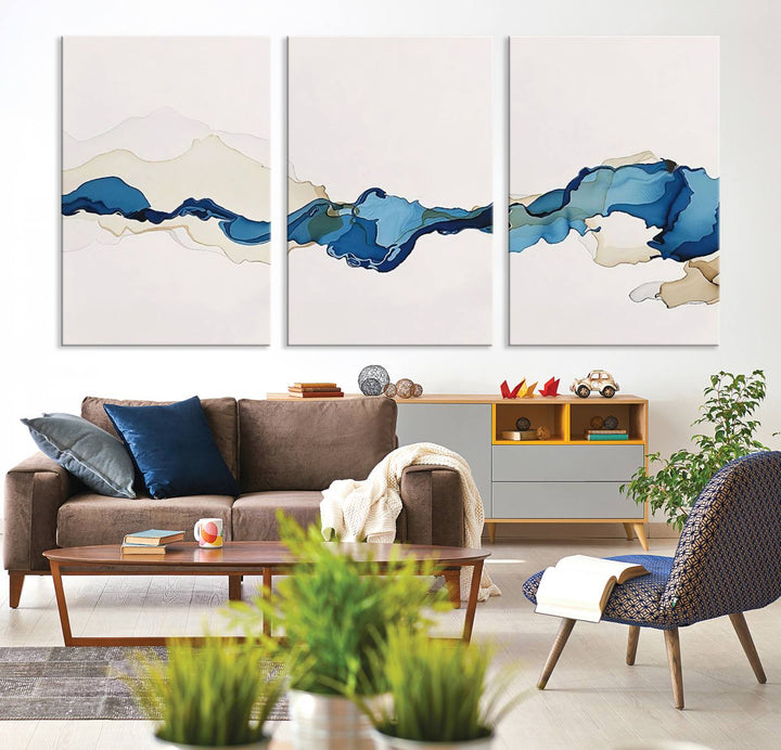 The modern living room showcases a set of three canvas prints with abstract blue art on museum-quality materials.