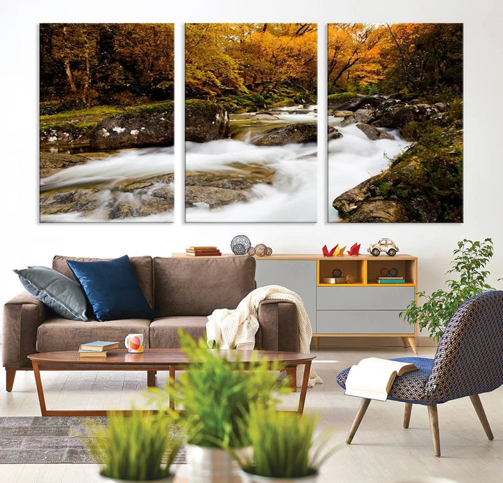 The living room is adorned with the "Wall Art Waterfall Canvas Print River in Forest in Autumn," a triptych on museum-quality canvas showcasing a flowing river surrounded by autumn trees. This ready-to-hang artwork features a UV-protective coating to ensure enduring vibrancy.