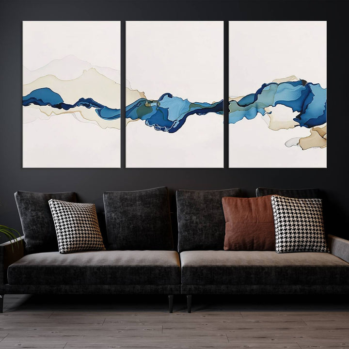 The modern living room showcases a set of three canvas prints with abstract blue art on museum-quality materials.