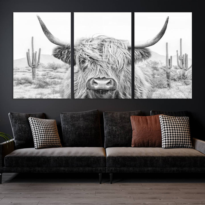 The "Rustic Charm | Cow Longhorn Black White Bighorn Wall Art Canvas Print" is a stunning triptych that showcases a highland cow with long horns set against a desert landscape with cacti in the background. This farmhouse wall art elevates any room into a rustic haven with its gallery-quality canvas.