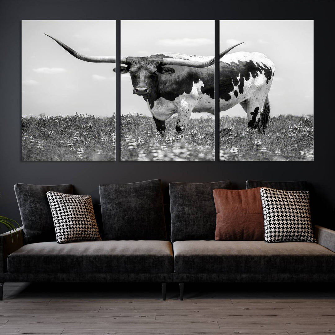 The Texas Black White Highland Longhorn Cow Wall Art Canvas Print, a gallery-quality triptych, elegantly adorns the wall, showcasing a striking black-and-white depiction of a longhorn cow in a field.